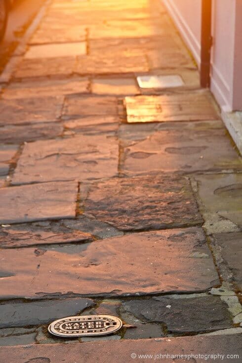 Like many old cities, Charleston has wonderful street surfaces. It's part of the city, so show that, but make it interesting. This may look like a snapshot but it's anything but. Long morning light gives dramatic colour, but even more importantly, the low angle side lighting shows the texture of the flag stones. I placed the inspection cover to anchor the shot and the drain pipe to pull your eye through it.