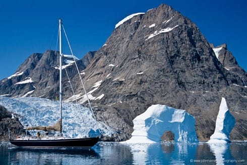 "Morgan's Cloud", a McCurdy and Rhodes 56' cutter, seen beside an arch berg with glacier and mountain behind, a typical East Greenland scene. The icecap reaches down to the sea in numerous glaciers and there are a floating profusion of bergs and smaller pieces of ice to be carefully avoided.