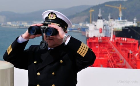 A captain looking through binoculars on the deck of a ship.